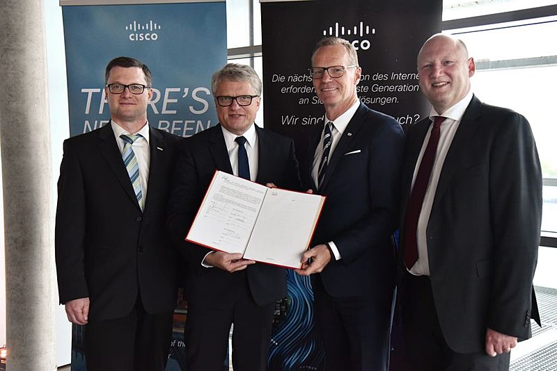 Vier Männer halten eine Mappe in die Kamera zur Verdeutlichung der Zusammenarbeit von LINZ AG TELEKOM und Cisco.